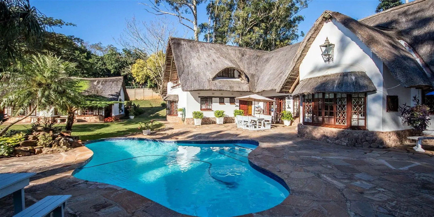 Large house with a thatched roof and a swimming pool in a garden setting
