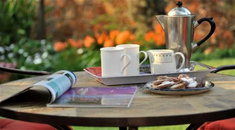 Outdoor table with coffee pot cups pastries and a magazine in a garden