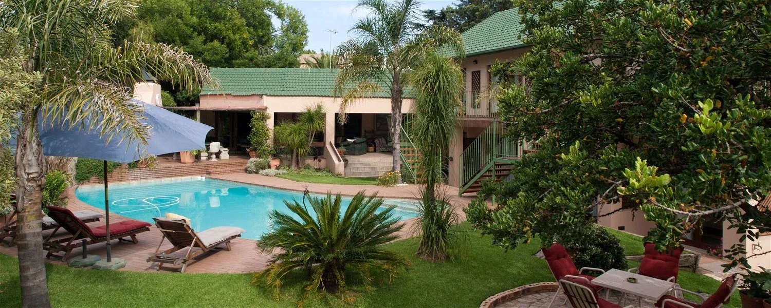 Swimming pool with lounge chairs umbrellas and a house in a lush garden
