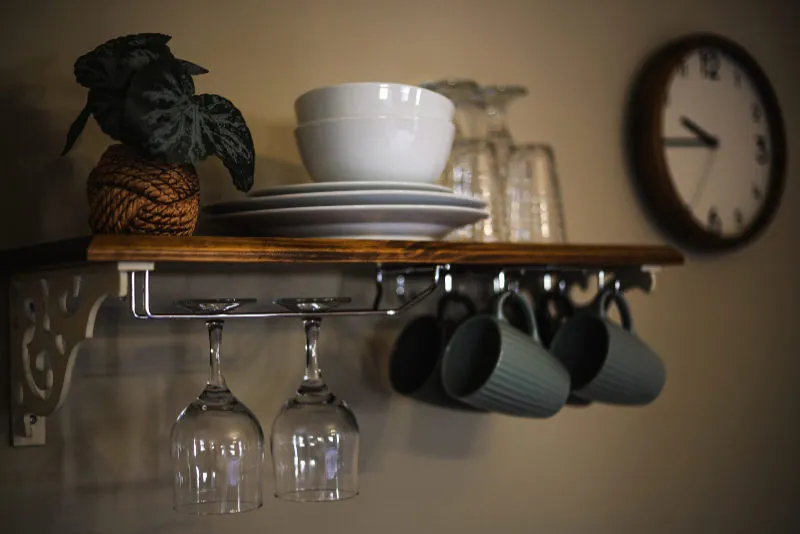 Wooden shelf with dishes mugs wine glasses plant and wall clock