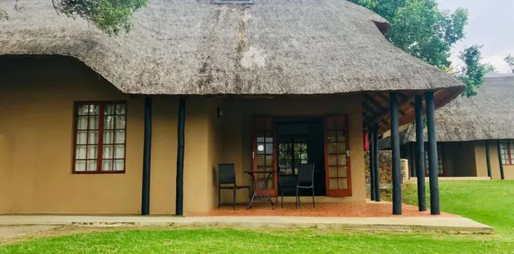 Traditional thatchedroof cottage with veranda and chairs in a grassy area