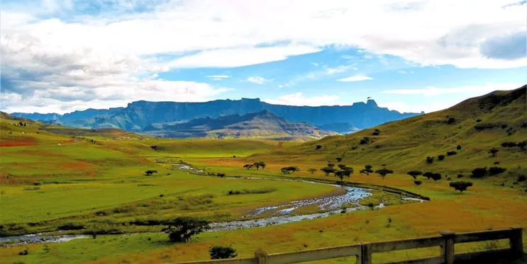 Lush green valley with a river mountains in the background and a wooden fence