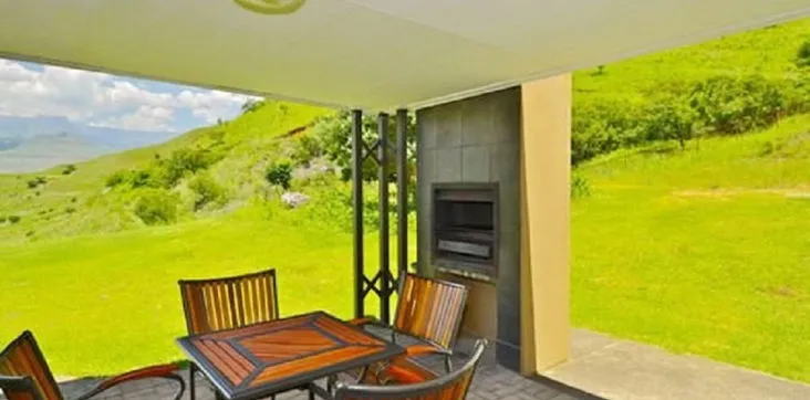 Outdoor patio with wooden table and chairs overlooking a green hillside