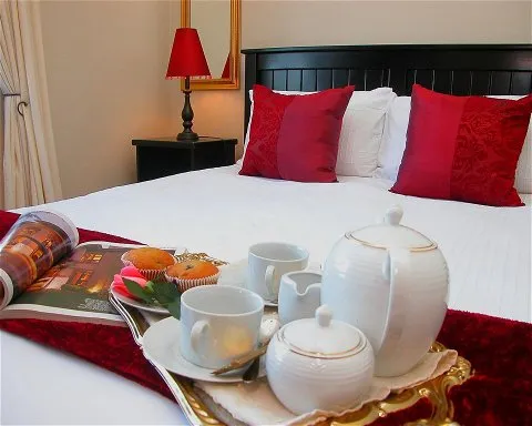 Bed with red pillows breakfast tray with tea set and muffins bedside lamp