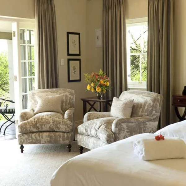 Bedroom with two armchairs a bed and open curtains revealing a garden view
