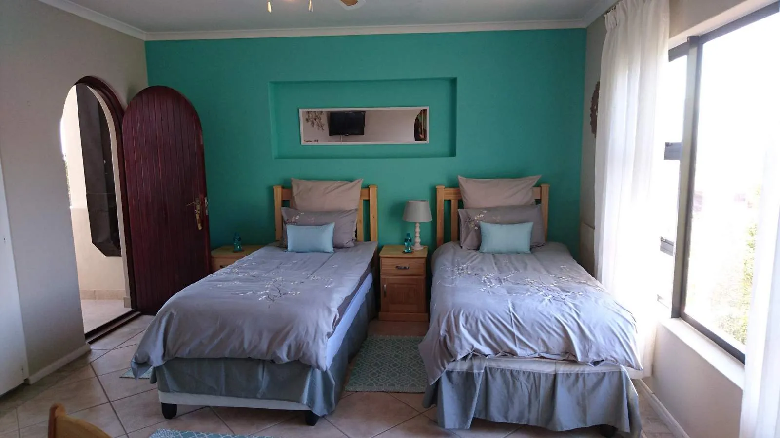 Two single beds in a tidy bedroom with teal walls and a large window
