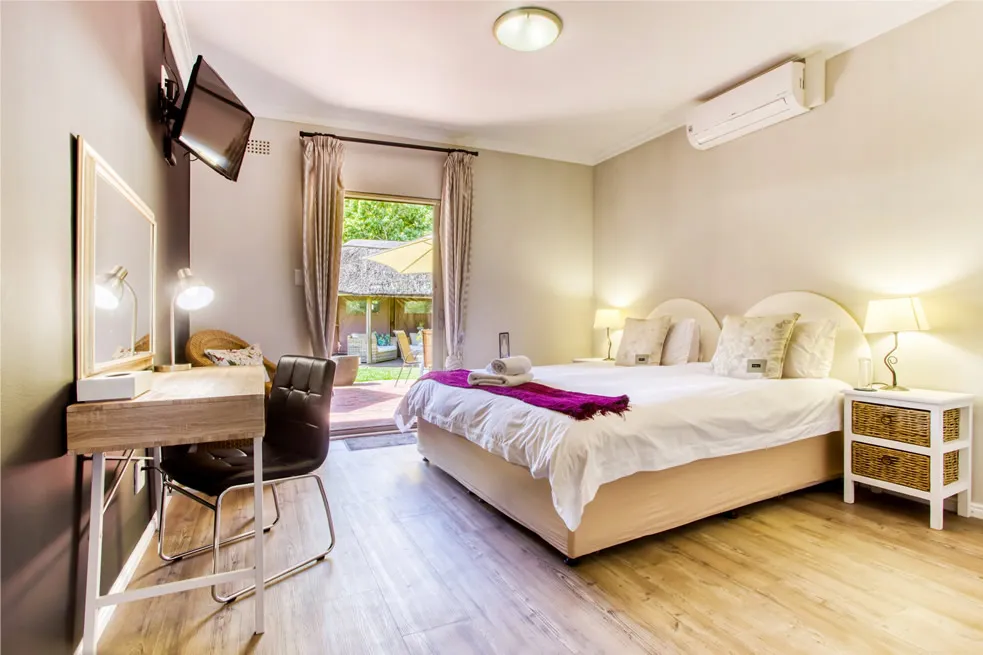 Modern bedroom with large bed desk TV and garden view through glass doors