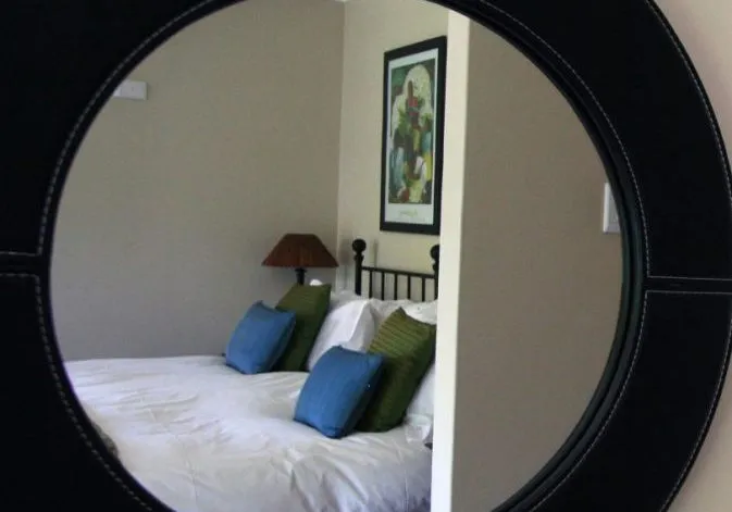 Reflection of a bed with pillows and a framed picture in a round mirror