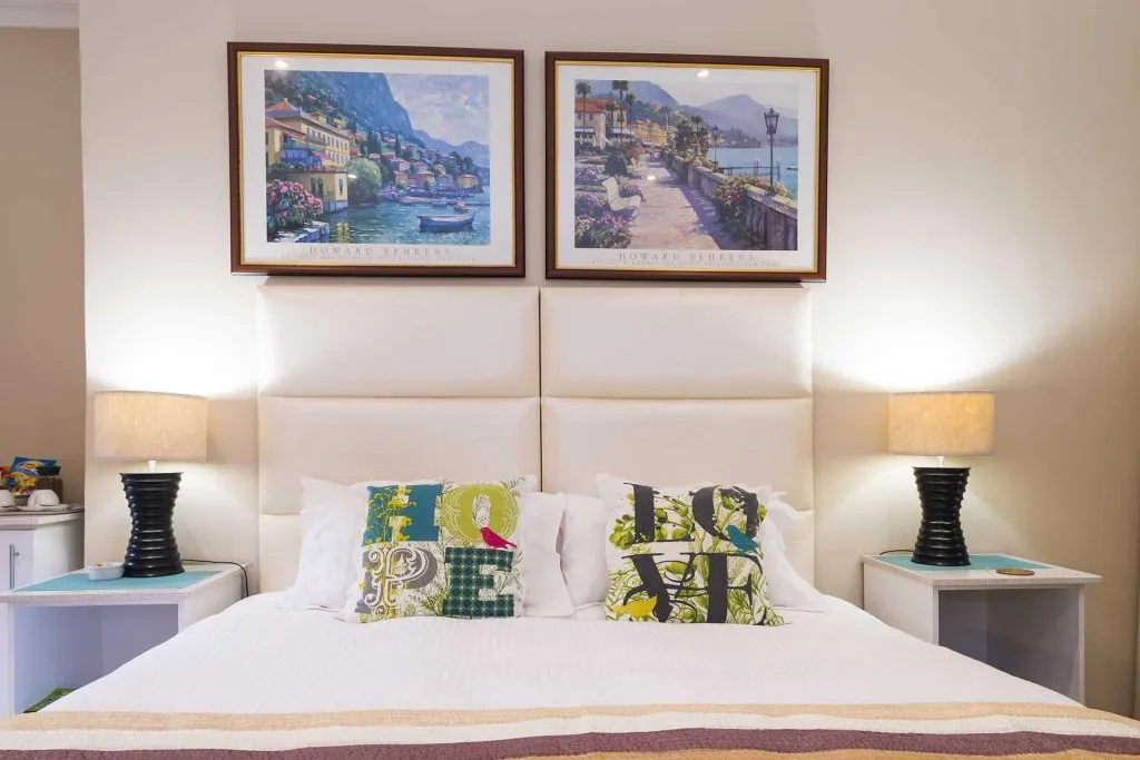 Bedroom with two framed paintings above a bed with colorful pillows and lamps
