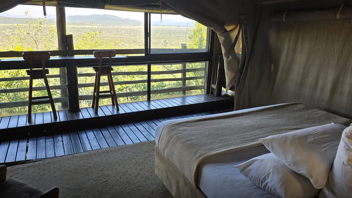 Bed in a tent with a view of a wooden deck and landscape