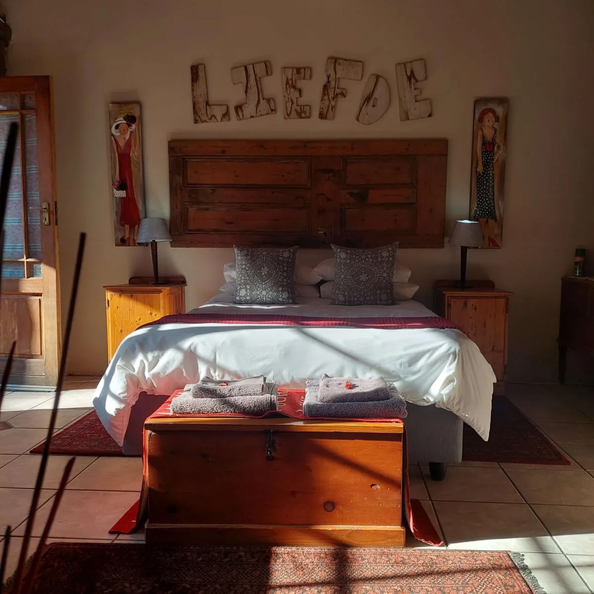 Wooden bed with white linens decorative pillows and a wooden chest at the foot