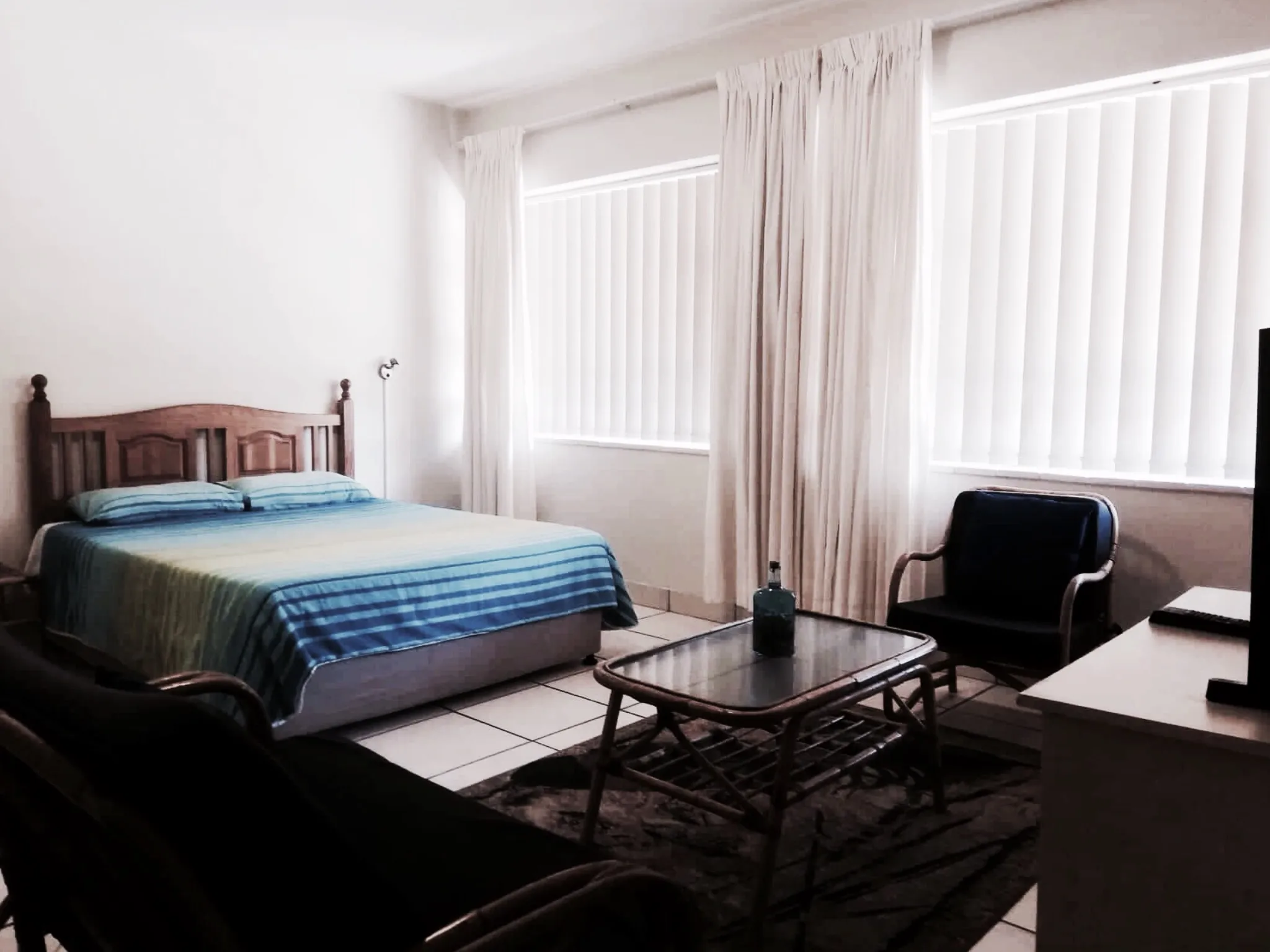 Bedroom with bed chair table and TV bright with white curtains