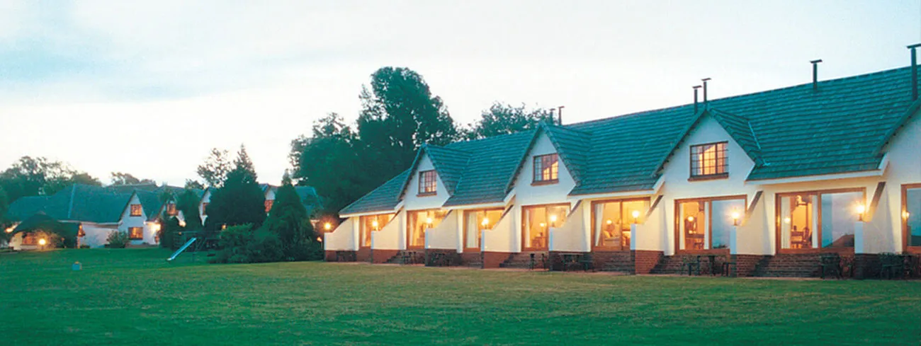 Row of cozy lit cottages in a grassy field during twilight