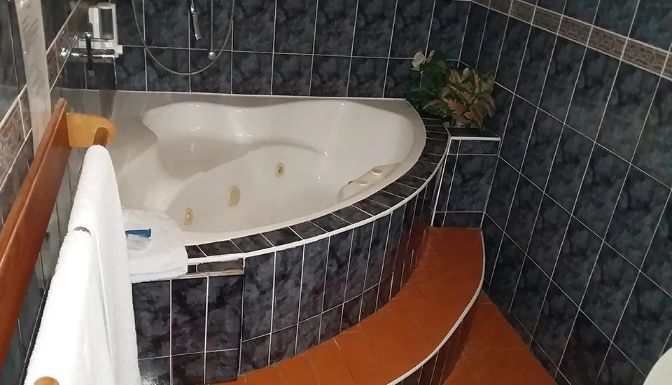 Jacuzzi tub with steps tiled walls and a towel on a rack