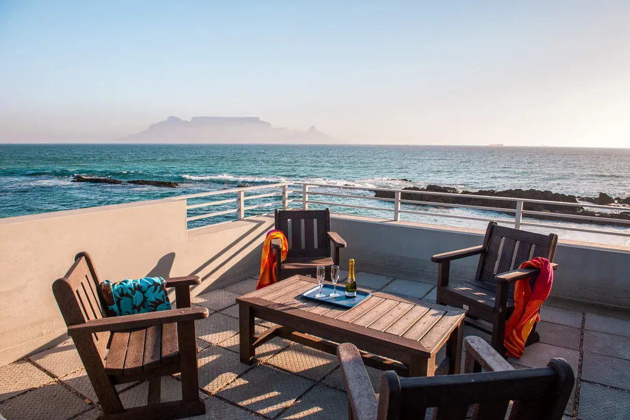 Wooden chairs and table on a patio overlooking the ocean with distant mountains