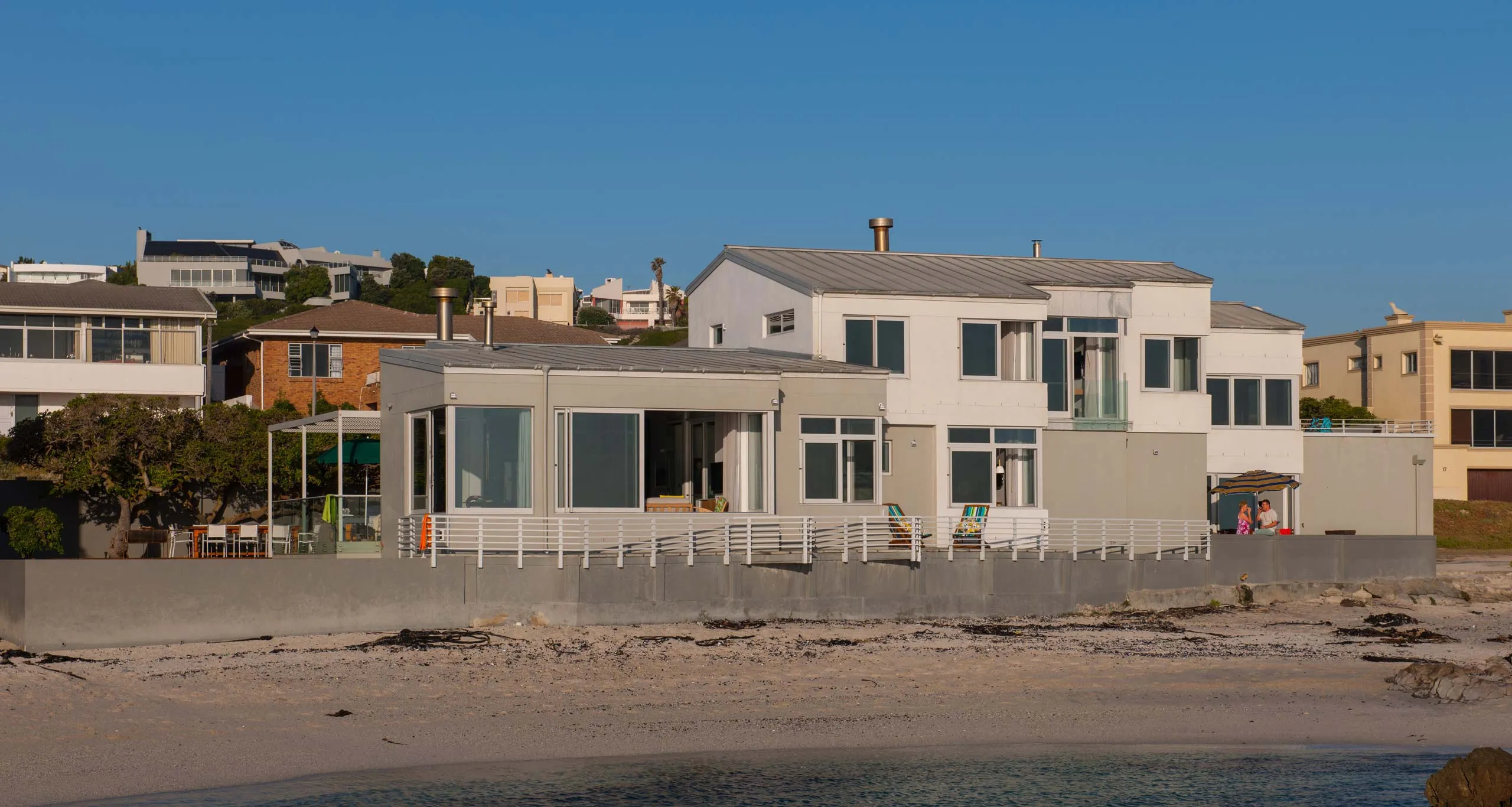 Modern beachfront houses with large windows on a sandy shore under a clear sky