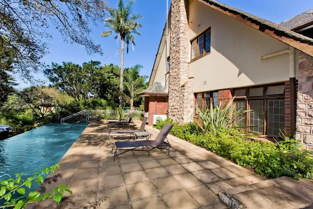 Swimming pool with lounge chairs beside a large house with stone and stucco exterior