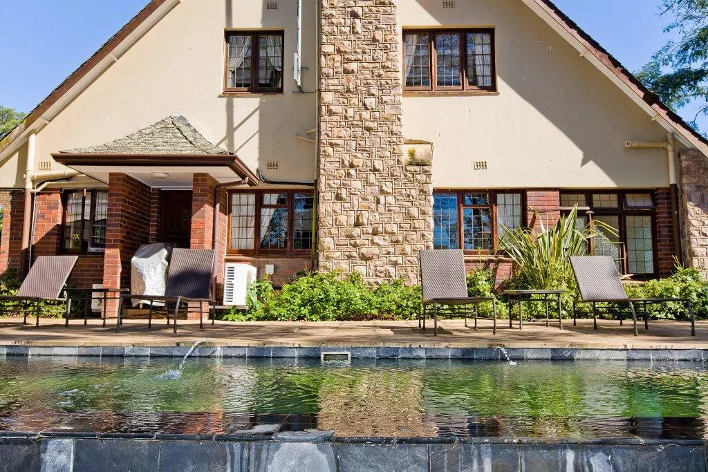 House with stone chimney pool in foreground and lounge chairs by the pool