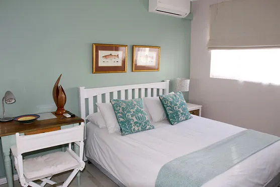 Bedroom with white bed teal pillows desk and window blinds on green walls