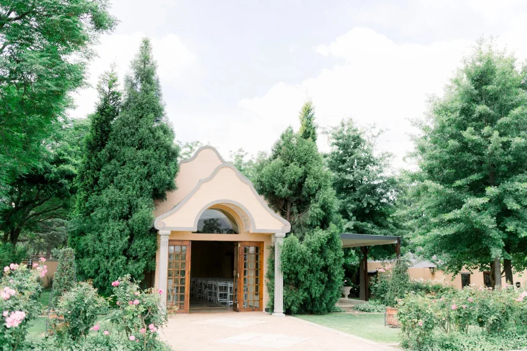 Small chapel entrance surrounded by greenery and flowers on a sunny day