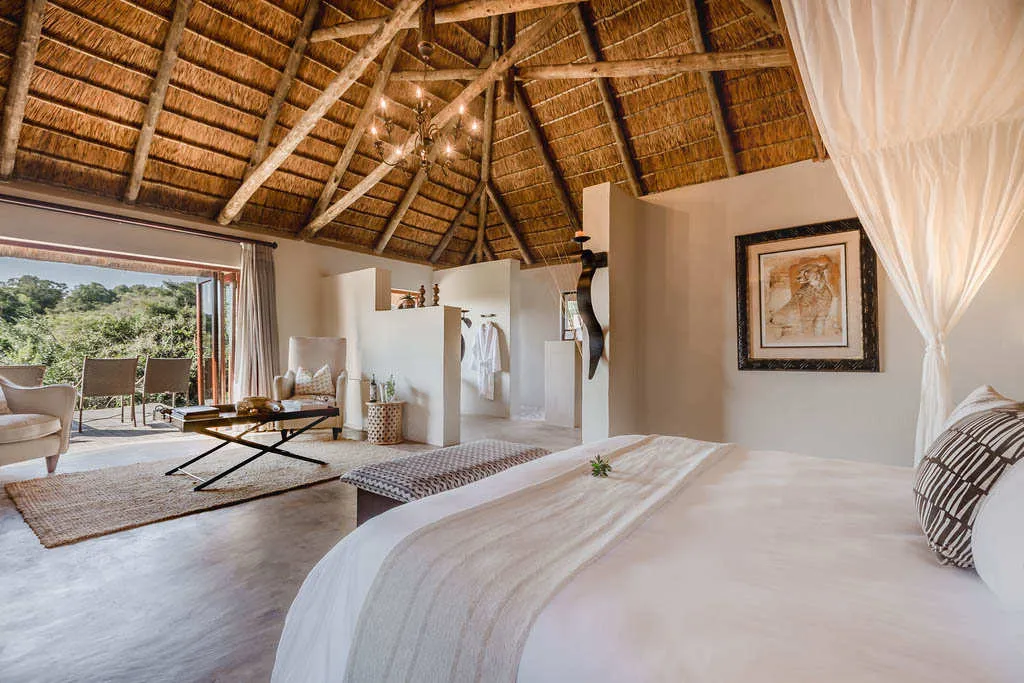 Luxury bedroom with thatched roof open to outdoor seating area with forest view