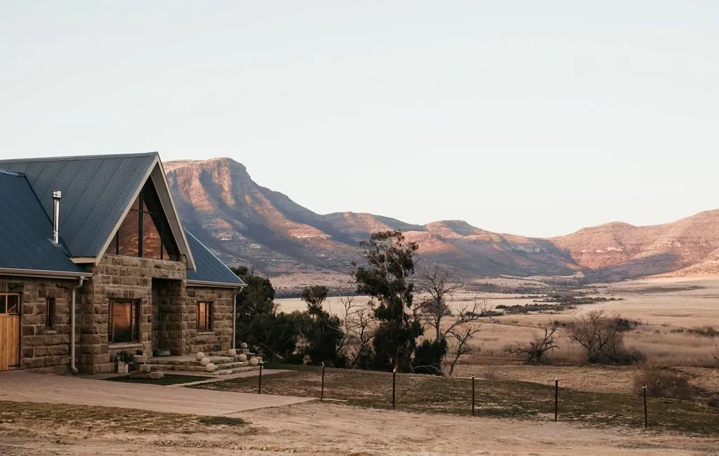 Stone house with blue roof in front of mountains and open fields