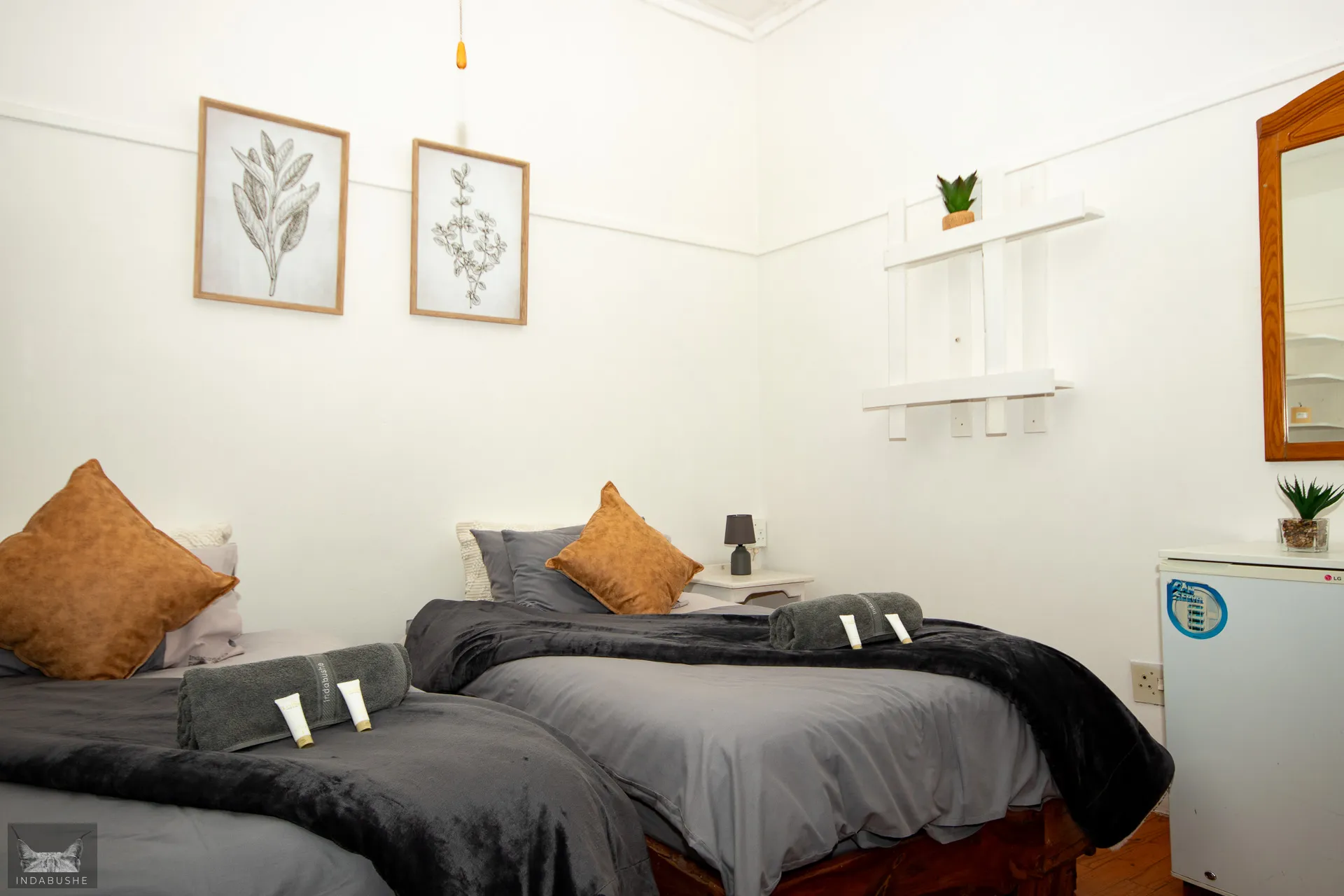 Two single beds in a tidy whitewalled room with artwork and a small fridge