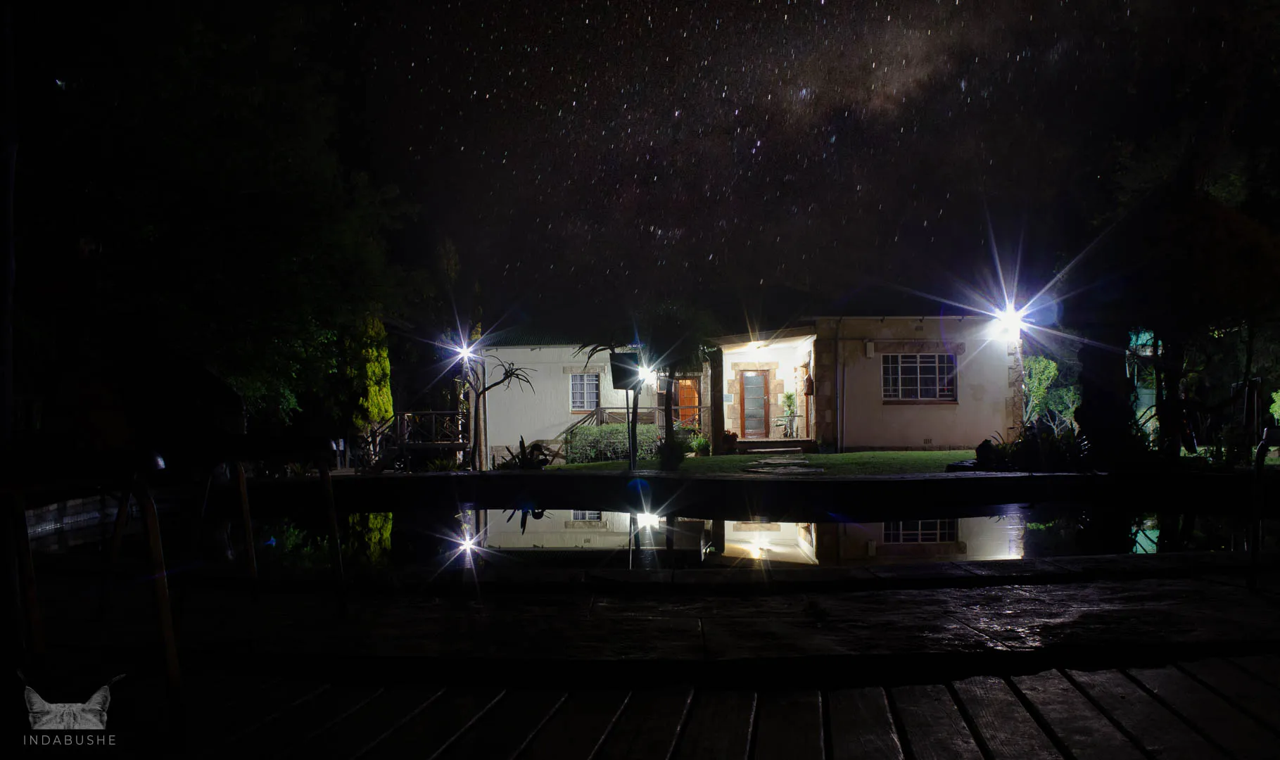House at night with bright stars reflected in a pool surrounded by trees