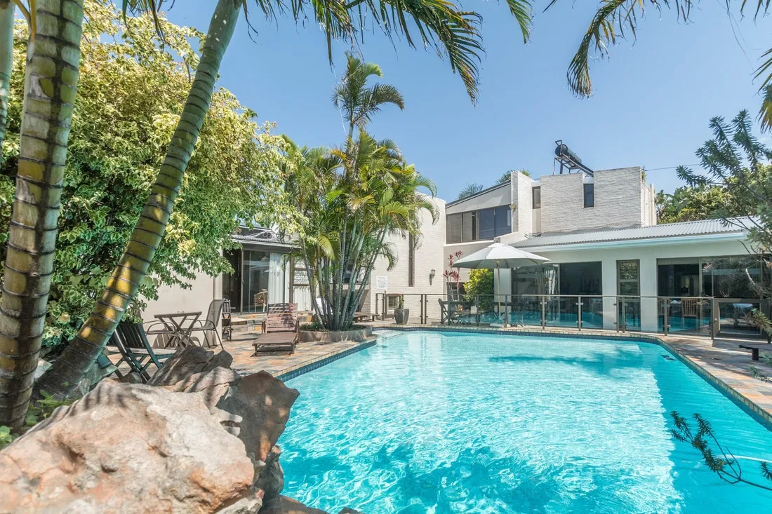 Swimming pool with lounge chairs palm trees and modern house in the background