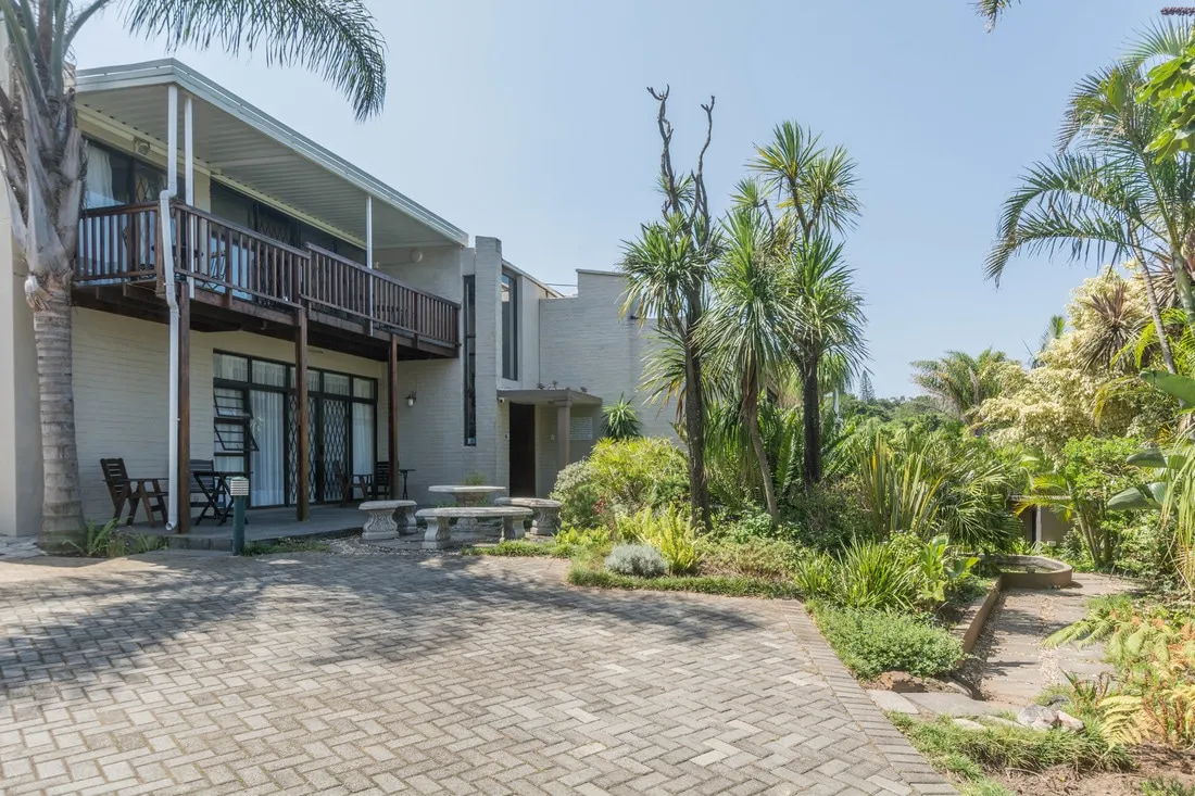 Modern twostory house with balcony surrounded by lush tropical plants and palm trees