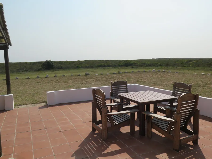 Wooden table and chairs on a tiled patio with open fields in the background