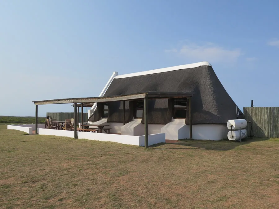 A thatchedroof house with a veranda in a grassy area under a blue sky