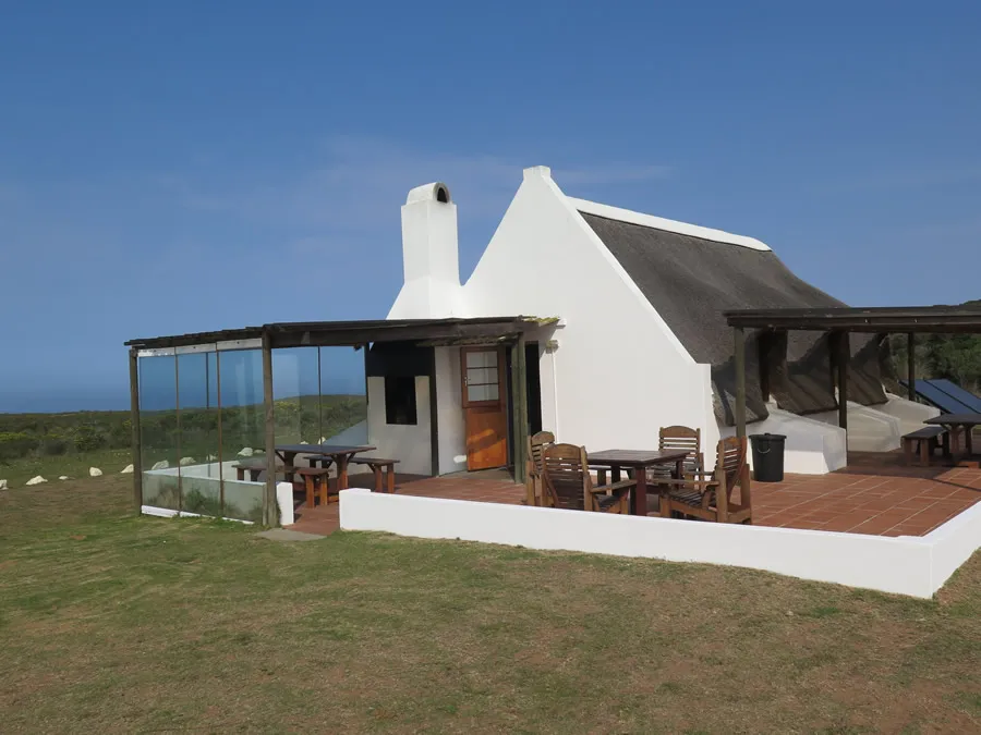 White cottage with a thatched roof outdoor seating and ocean view