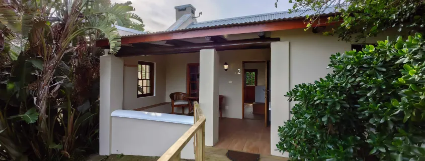 Cottage with open door surrounded by greenery and a wooden fence