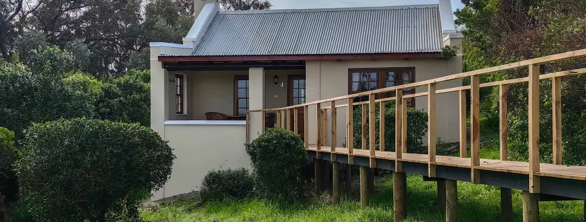 House with a wooden walkway leading to it surrounded by greenery
