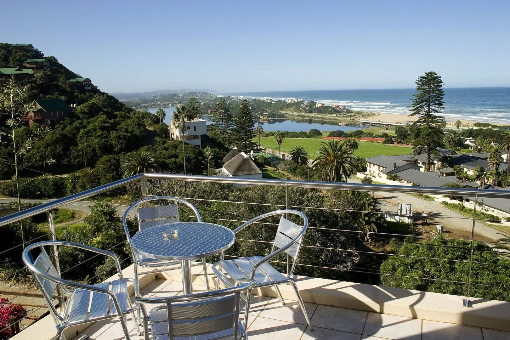 Outdoor patio with table and chairs overlooking a coastal landscape with greenery and ocean