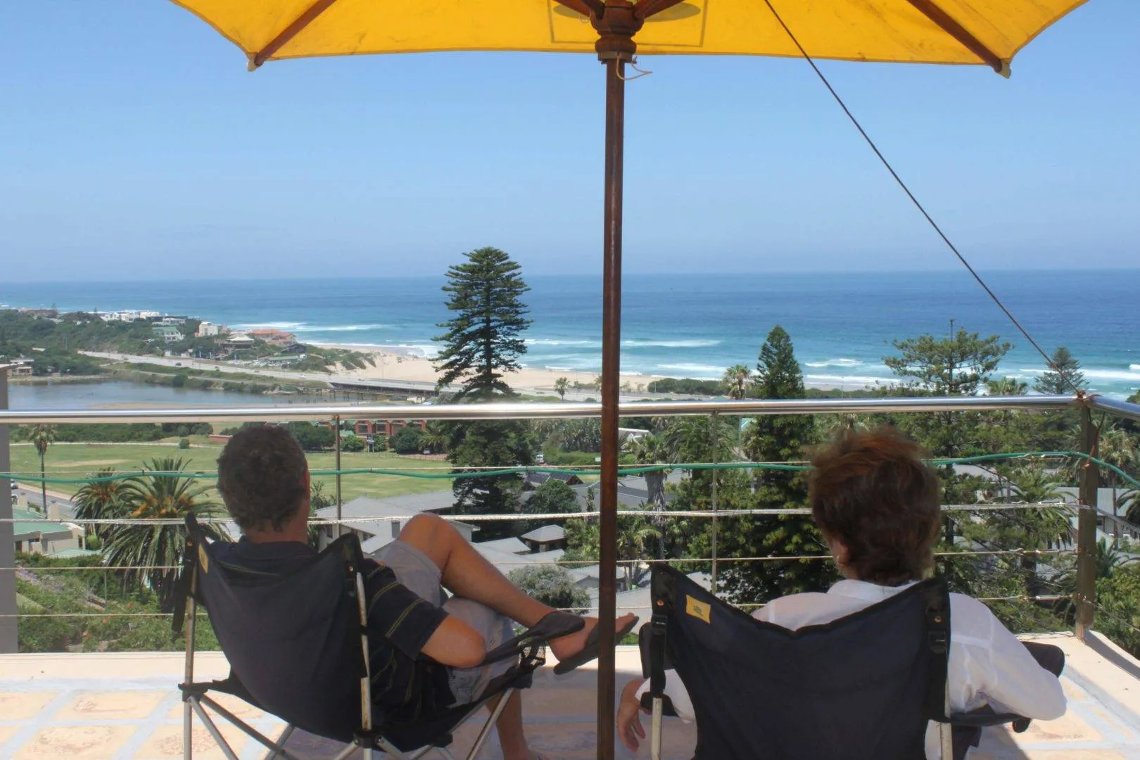 Two people relaxing on deck chairs overlooking a beach and ocean