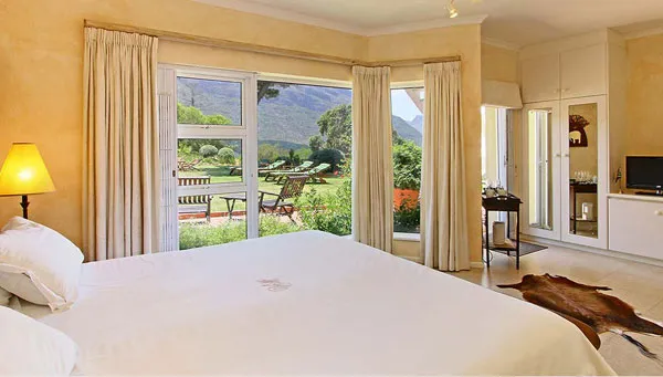 Bedroom with large windows overlooking a garden and mountains with a bed and lamp