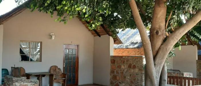 Cottage with wooden door stone wall and tree providing shade in outdoor setting