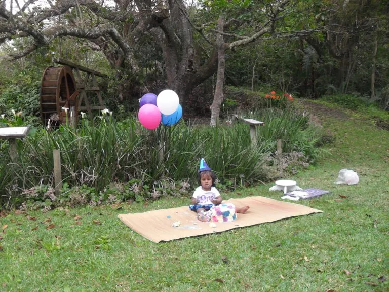 Child in party hat on a mat with balloons in a garden setting