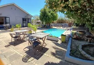 Swimming pool with patio furniture surrounded by plants and a house in the background