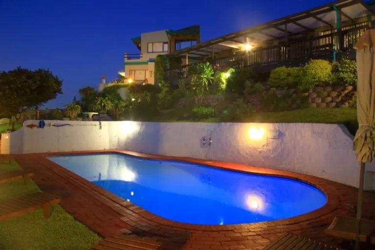 Night view of an illuminated swimming pool with surrounding buildings and vegetation