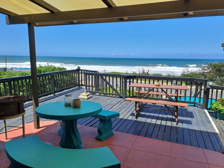 Wooden deck with turquoise furniture overlooking ocean and sandy beach