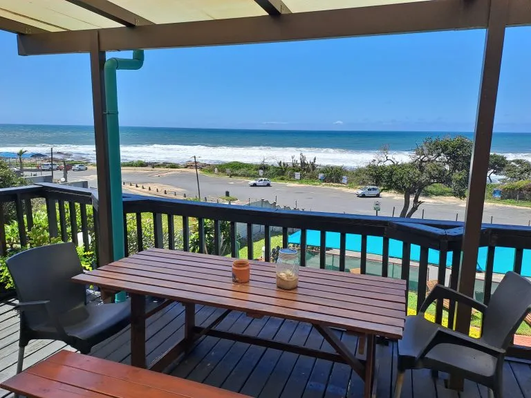 Wooden deck with table and chairs overlooking a beach and ocean