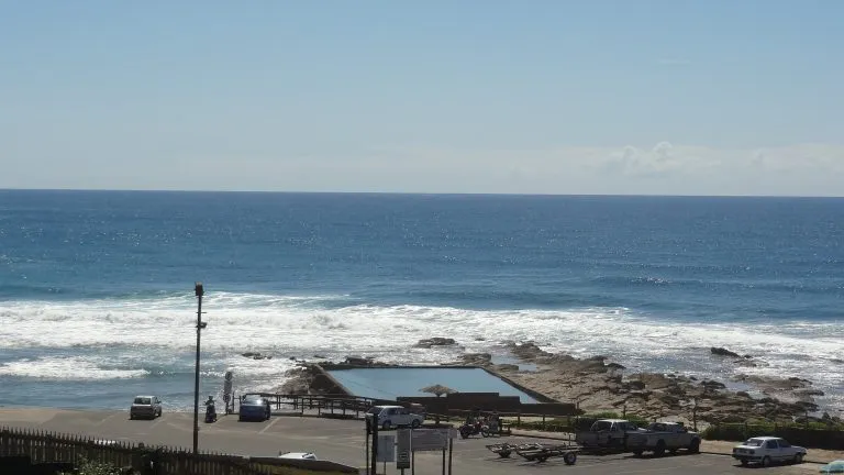 Ocean view with rocky shore parked cars and a small building in the foreground
