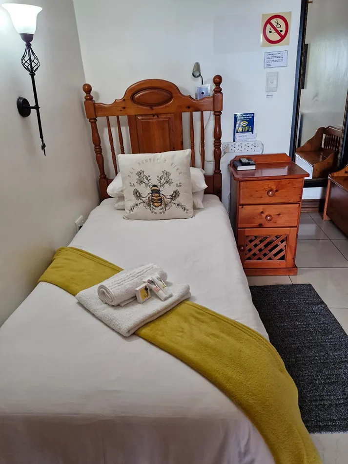 Single bed in a small room with wooden furniture and a bedside lamp
