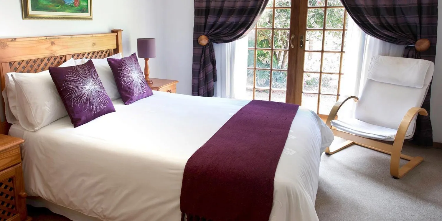 Bedroom with large bed purple pillows and armchair near a window with curtains