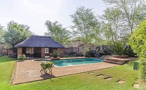 Swimming pool with a thatchedroof hut and lush greenery in a backyard