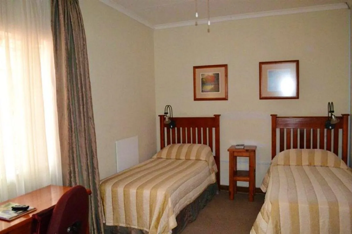 Twin beds in a simple welllit bedroom with wooden furniture and wall art