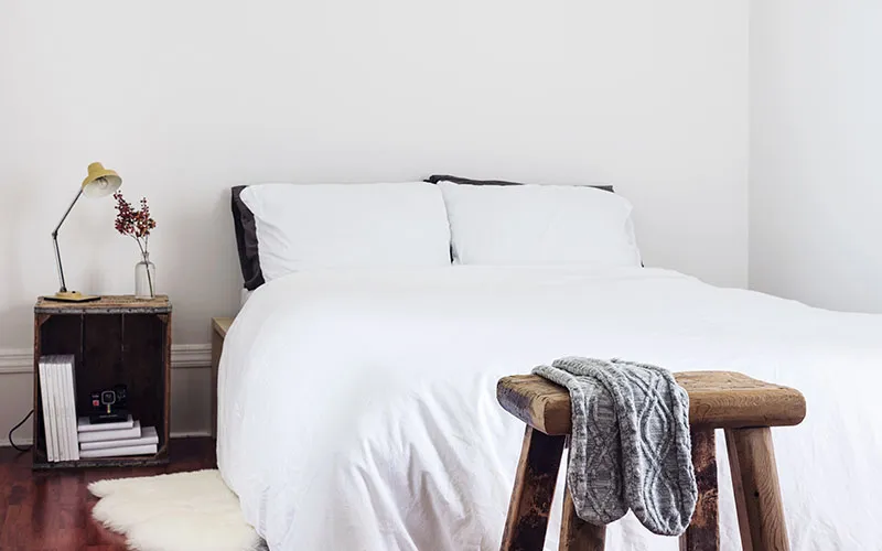 White bed with wooden nightstand and stool in a minimalist bedroom
